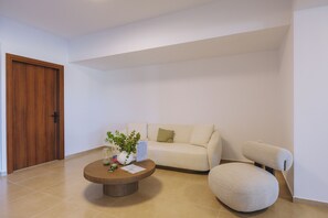 Un salon moderne avec une porte en bois, un canapé beige, une table basse ronde et un petit pouf rond.