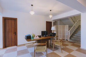 Une pièce avec un bureau en bois, deux fauteuils en osier, un globe terrestre, une lampe et un escalier.