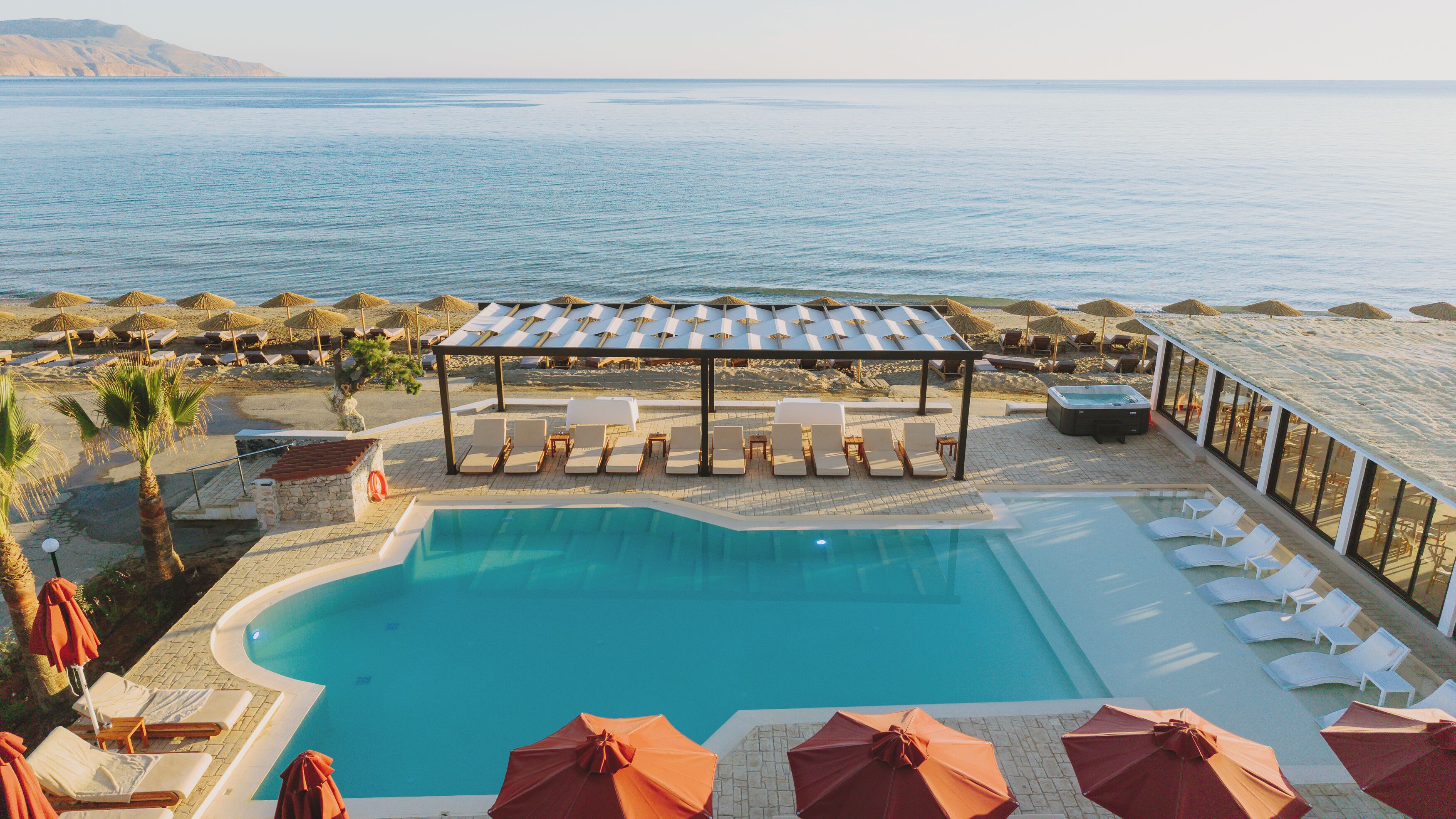 Un área de piscina con sillones de descanso y sombrillas, un jacuzzi y vistas al mar.
