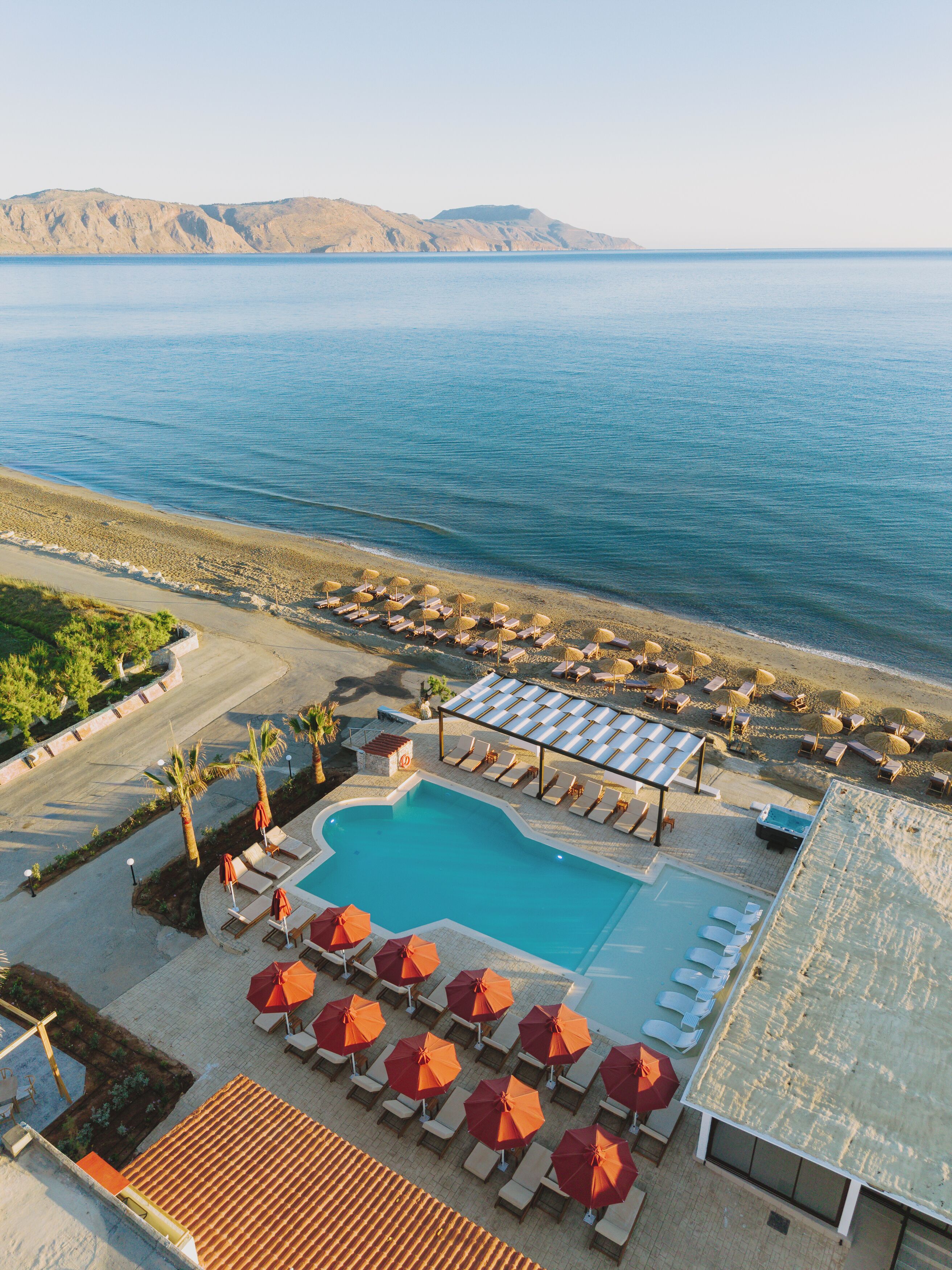 A resort with a swimming pool, sun loungers, umbrellas, and a view of the sea.