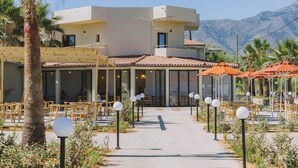 A modern building with a patio area, outdoor seating, and a mountain backdrop. - Casa di Notos Beach Hotel-Georgioupolis (Apokoronas)