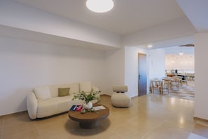 A modern living room with a sofa, coffee table, and a dining area with chairs and a table. - Casa di Notos Beach Hotel-Georgioupolis (Apokoronas)
