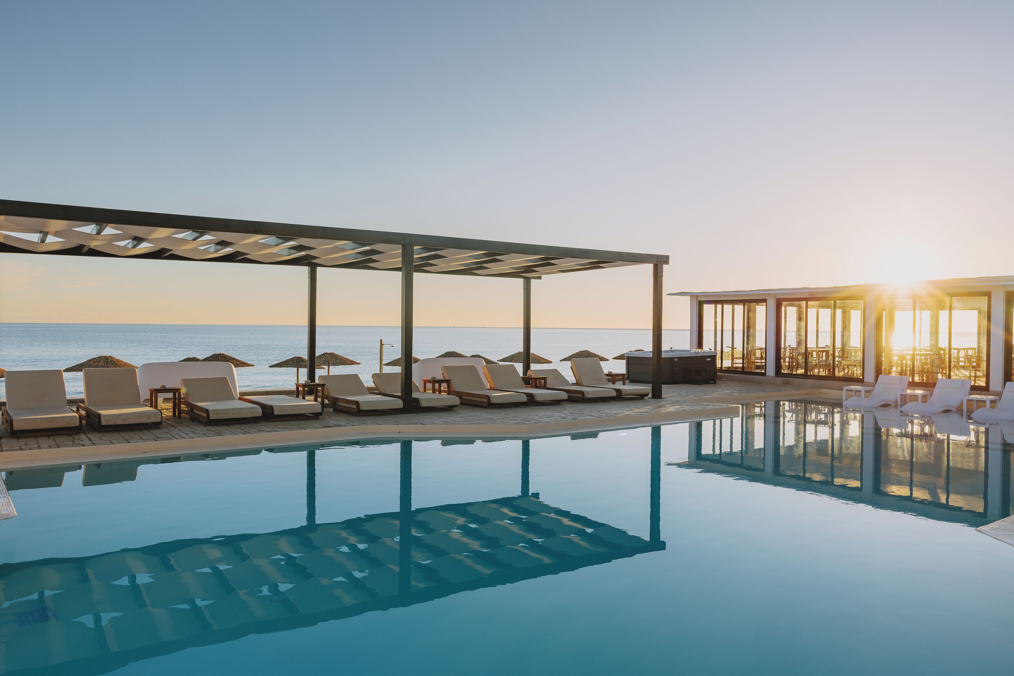 Una piscina con sillas de descanso y sombrillas, un área techada y vista al mar.