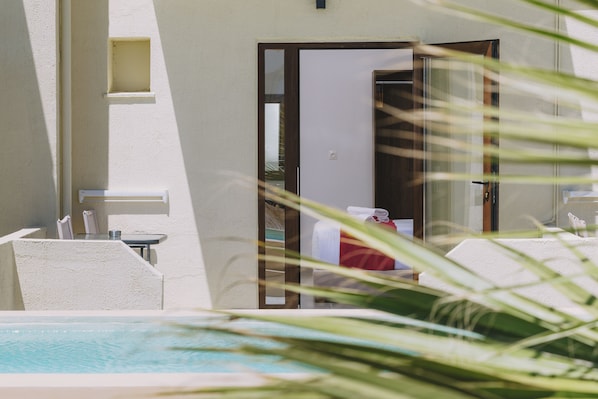 A poolside view with a door leading to a room, a small table, and a chair.