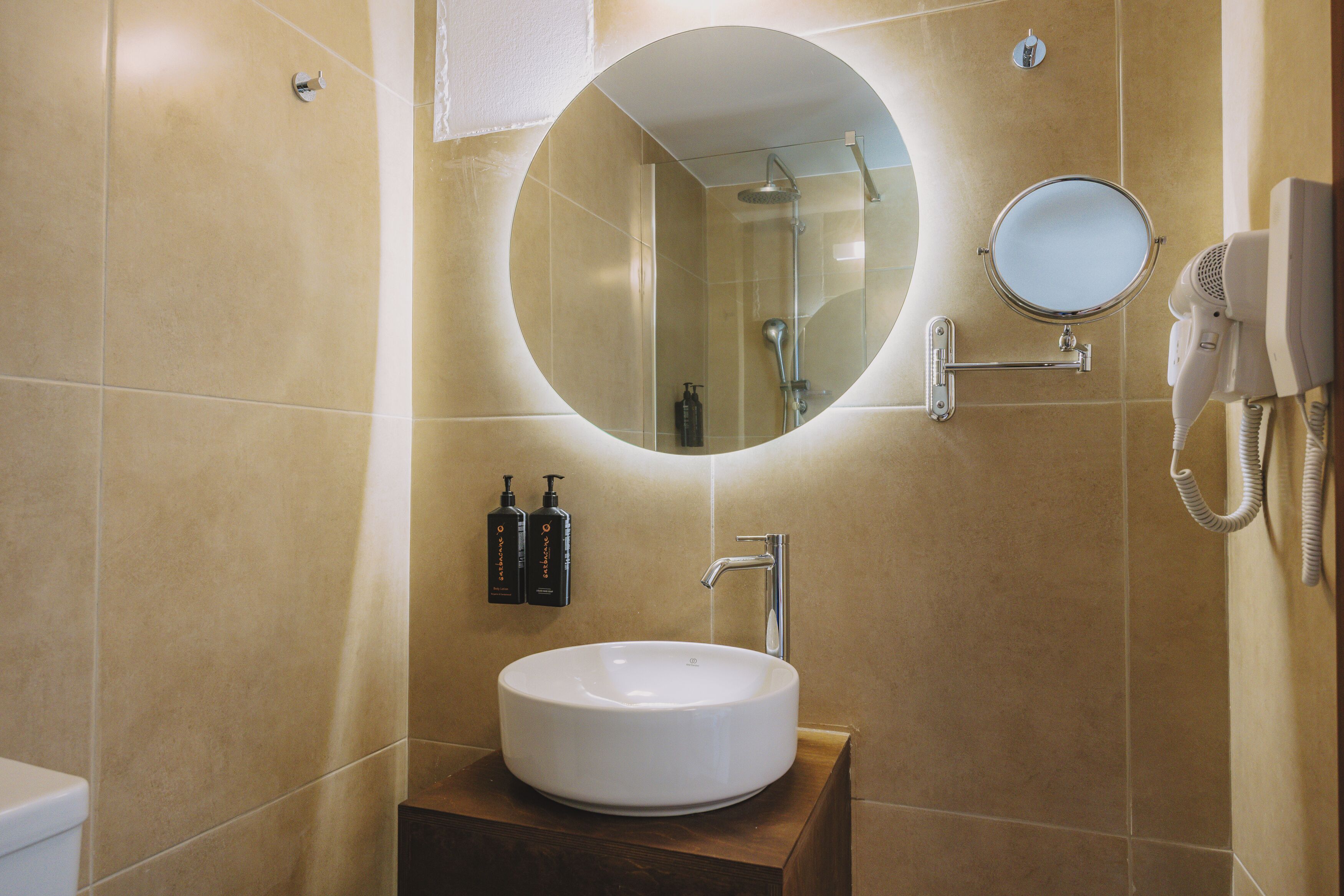 A bathroom with a round mirror, a sink, and a handheld hair dryer mounted on the wall.