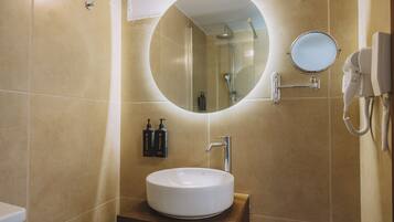 A bathroom with a round mirror, a sink, and a handheld hair dryer mounted on the wall.