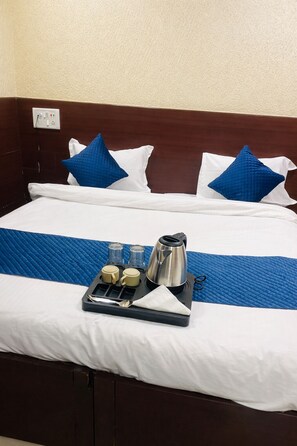 A neatly made bed with white and blue pillows, a blue bedspread, and a tray with a kettle, cups, and a spoon. - Hotel Glory By Seasons (Indore)
