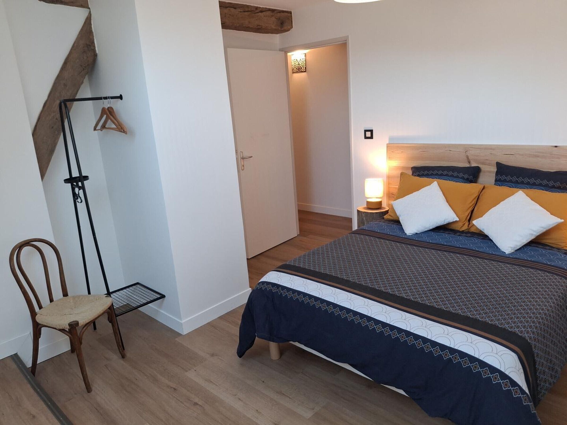 Een slaapkamer met een bed, een stoel, een kapstok en een deur naar een andere kamer.