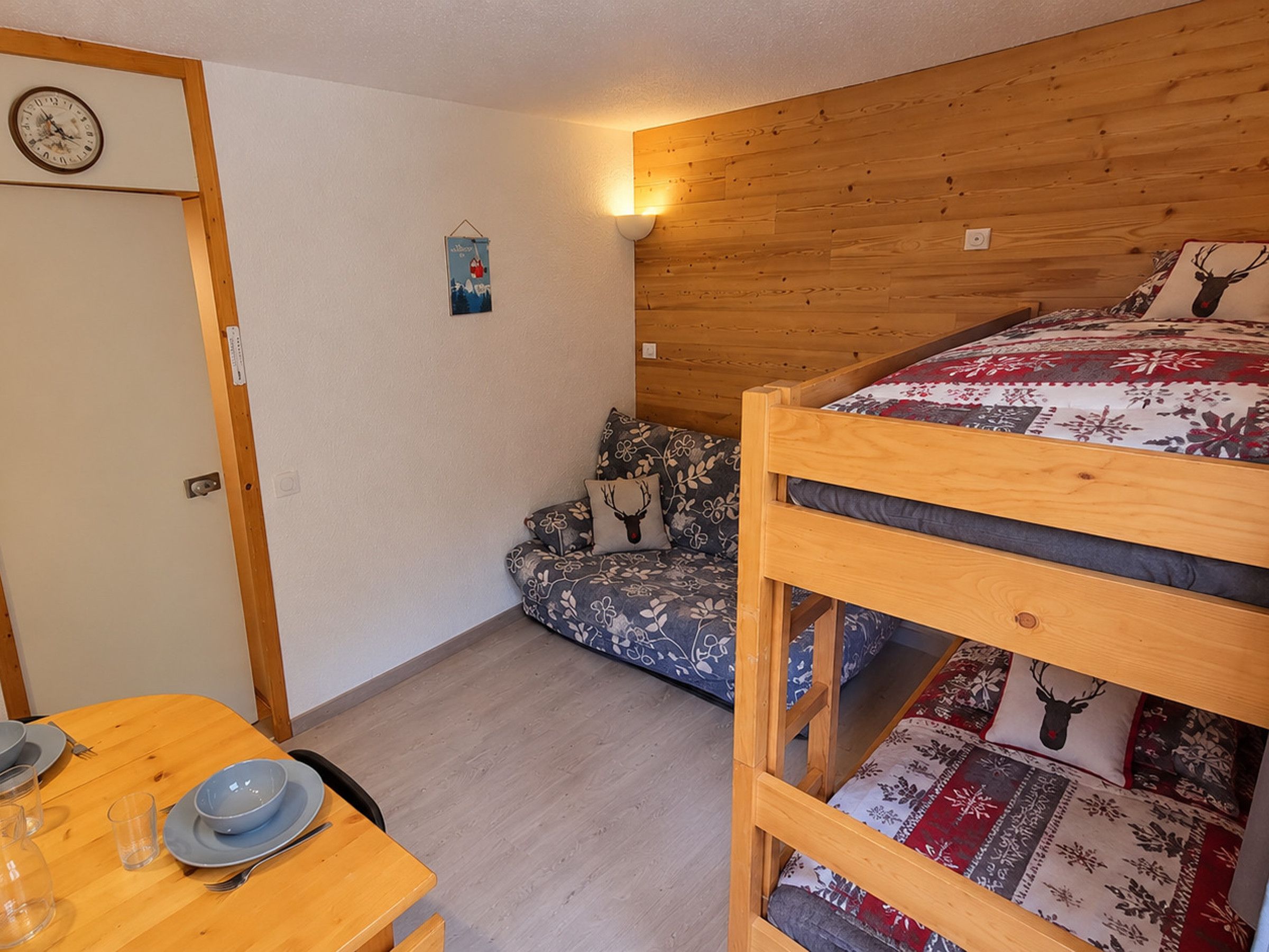 Une pièce avec un lit superposé, une petite table avec un bol et des verres, une horloge murale et un élément décoratif fixé au mur.