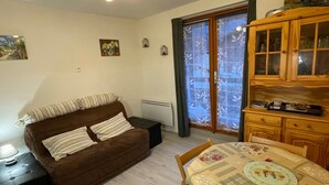 Una sala de estar acogedora con un sofá marrón, una mesa de comedor con mantel floreado y un mueble de madera con puertas de cristal.