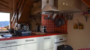 Una cocina con armarios blancos, encimera roja y estufa. Hay ollas colgadas en la pared y un lavabo con grifo.