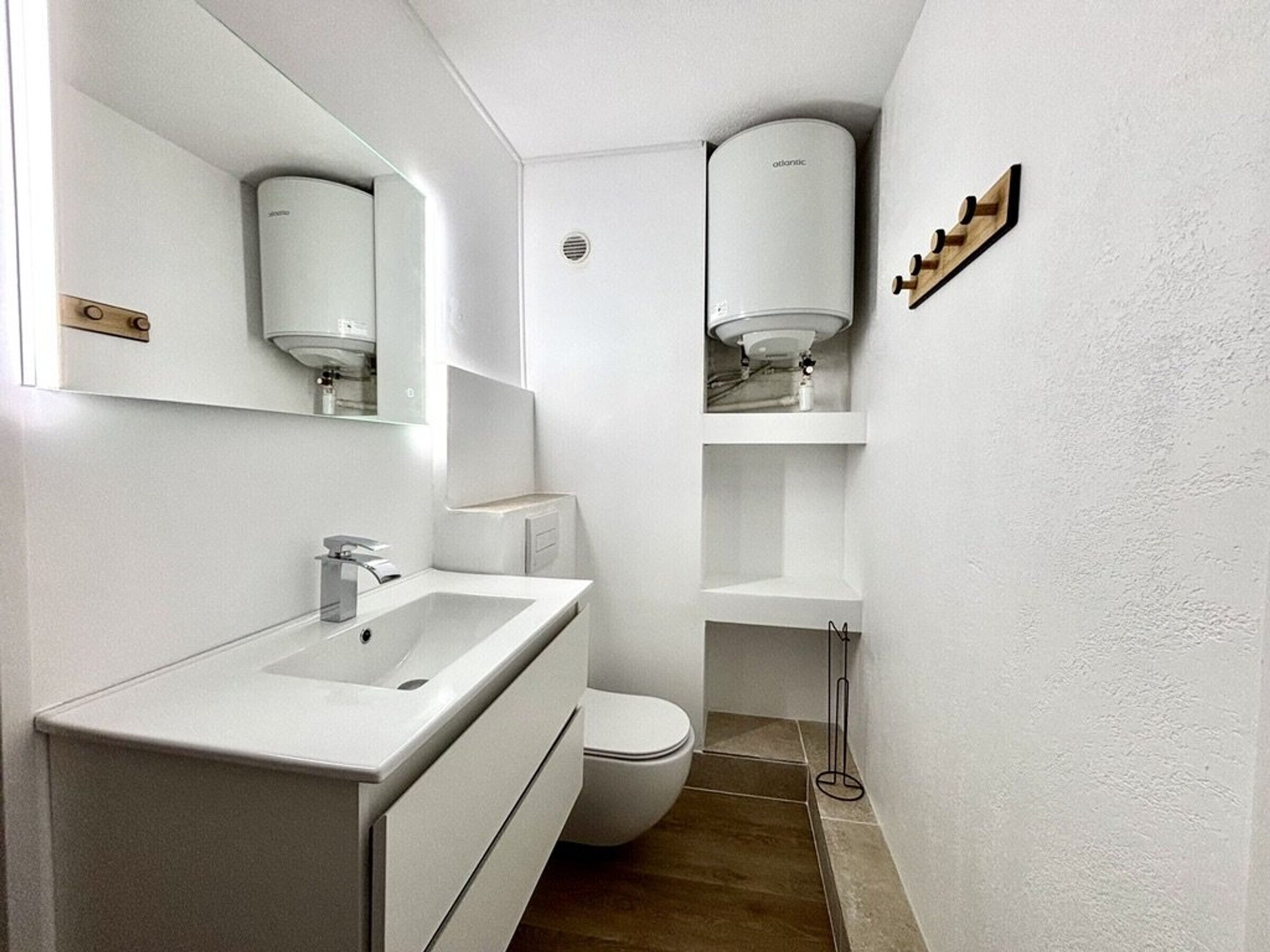 A modern bathroom with a white sink, mirror, toilet, and a wall-mounted toilet paper holder.