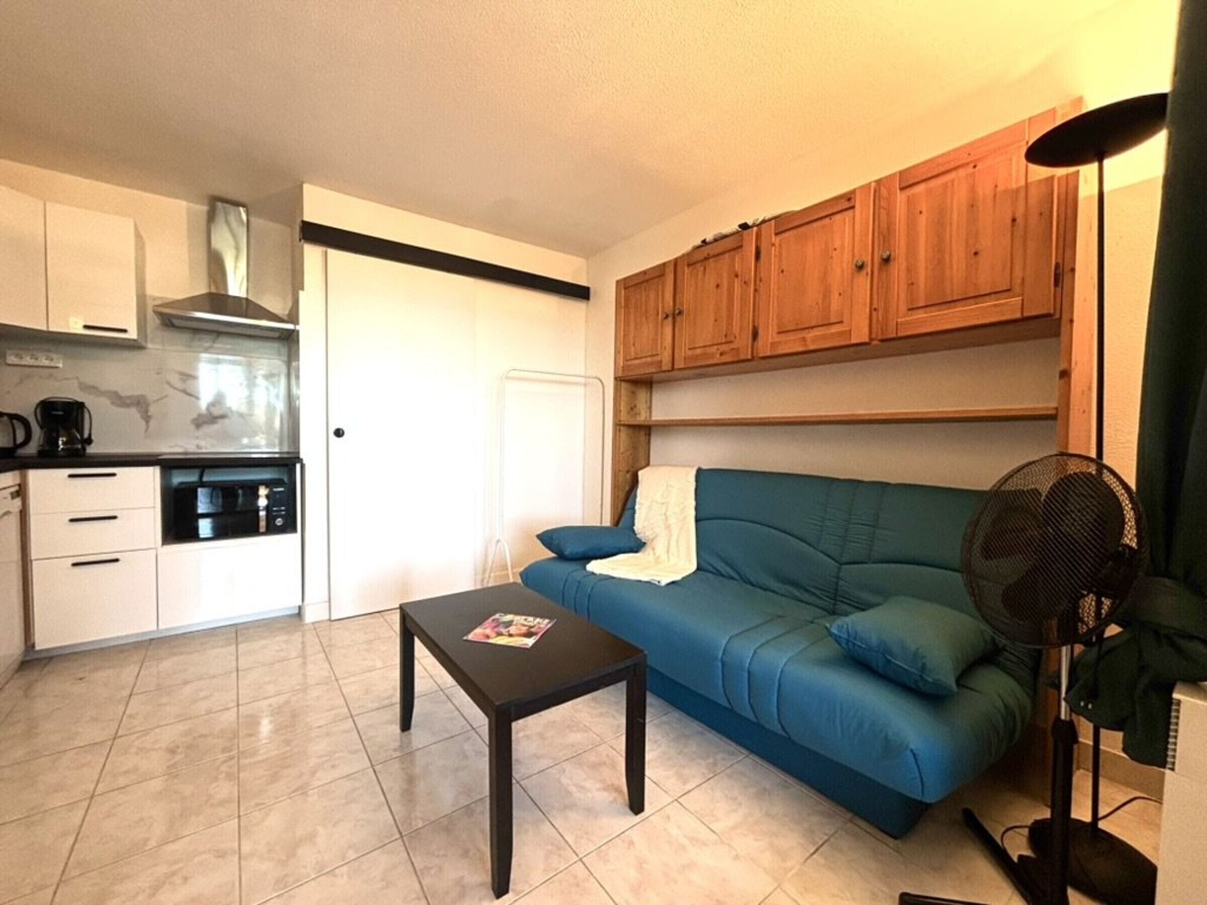 A compact living space with a kitchenette, a sofa, a coffee table, and a fan.