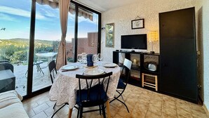 A dining area with a table set for four, a ceiling fan, a TV, and a sliding glass door leading to an outdoor patio. - Peaceful studio with pool in Cavalaire (Cavalaire-sur-Mer)