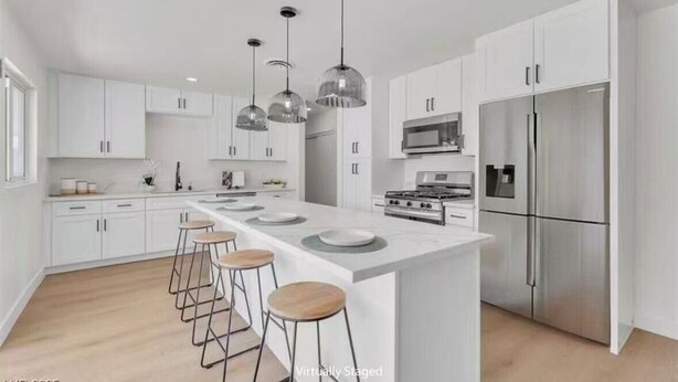 A modern kitchen with white cabinetry, a central island with stools, stainless steel appliances, and pendant lighting. - Beautiful 4-bedroom house with AC in enchanting Las Vegas (Las Vegas)