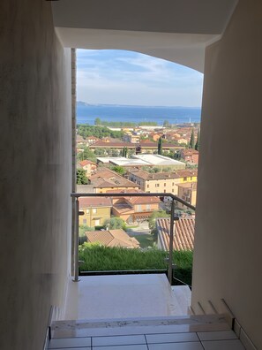 Blick vom Balkon auf einen klaren Himmel, ein entferntes Meer und eine Wohngegend mit Häusern.