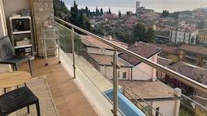 Un balcon offrant une vue sur un lac et la ville, aménagé avec des fauteuils et une table en osier.