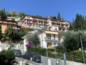 Ein mehrgeschossiges Wohnhaus mit Balkonen, einem Garten und einem geparkten Auto vor der Fassade.