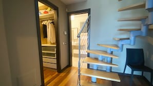 Un intérieur moderne avec un escalier en bois, un placard où sont suspendus des vêtements et une chaise.