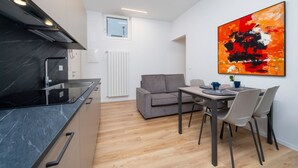 A compact kitchen with a black countertop and a grey sofa in a bright room with a large abstract painting. - GuestHost - Cozy 60 sqm apartment, located on the first floor of a building without an elevator.The accommodation is situated in a strategic location, allowing you to reach the main points of interest within a short walking distance or by public transpor (Udine)