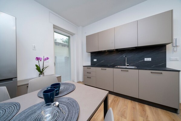 A modern kitchen with a black marble countertop, beige cabinets, and a dining area with a table set for two.