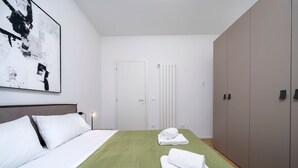 A hotel room with a bed, a green bedspread, white pillows, a white door, a radiator, and a large wardrobe. - GuestHost - Cozy 60 sqm apartment, located on the first floor of a building without an elevator.The accommodation is situated in a strategic location, allowing you to reach the main points of interest within a short walking distance or by public transpor (Udine)