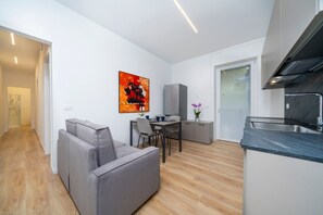 A modern apartment with a living area, dining space, kitchenette, and a door leading to a bathroom.