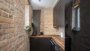 A narrow kitchen with exposed brick walls, dark cabinetry, and a wooden countertop. - Sunny 1BR Apartment near Park & Stadium (Riga)