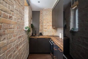 A narrow kitchen with exposed brick walls, dark cabinetry, and a wooden countertop. - Sunny 1BR Apartment near Park & Stadium (Riga)