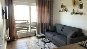 Un saló modern amb un sofà gris, una taula de centre i una làmpada de peu. Hi ha una porta corredissa de vidre que dona a un balcó.
