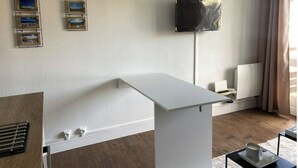 Un saló modern amb una taula blanca, un televisor penjat i quadres a la paret.