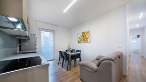 Een moderne keuken met een ingebouwde kookplaat, een eethoek met een tafel en stoelen, een bank en een schilderij aan de muur.