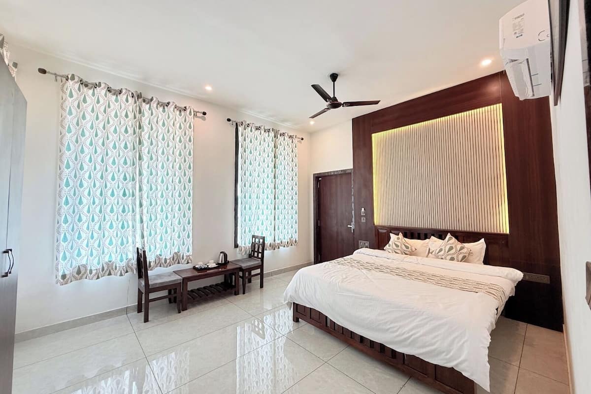 Quarto com uma cama grande, um ventilador de teto, uma cabeceira de madeira e uma janela com cortinas estampadas.
