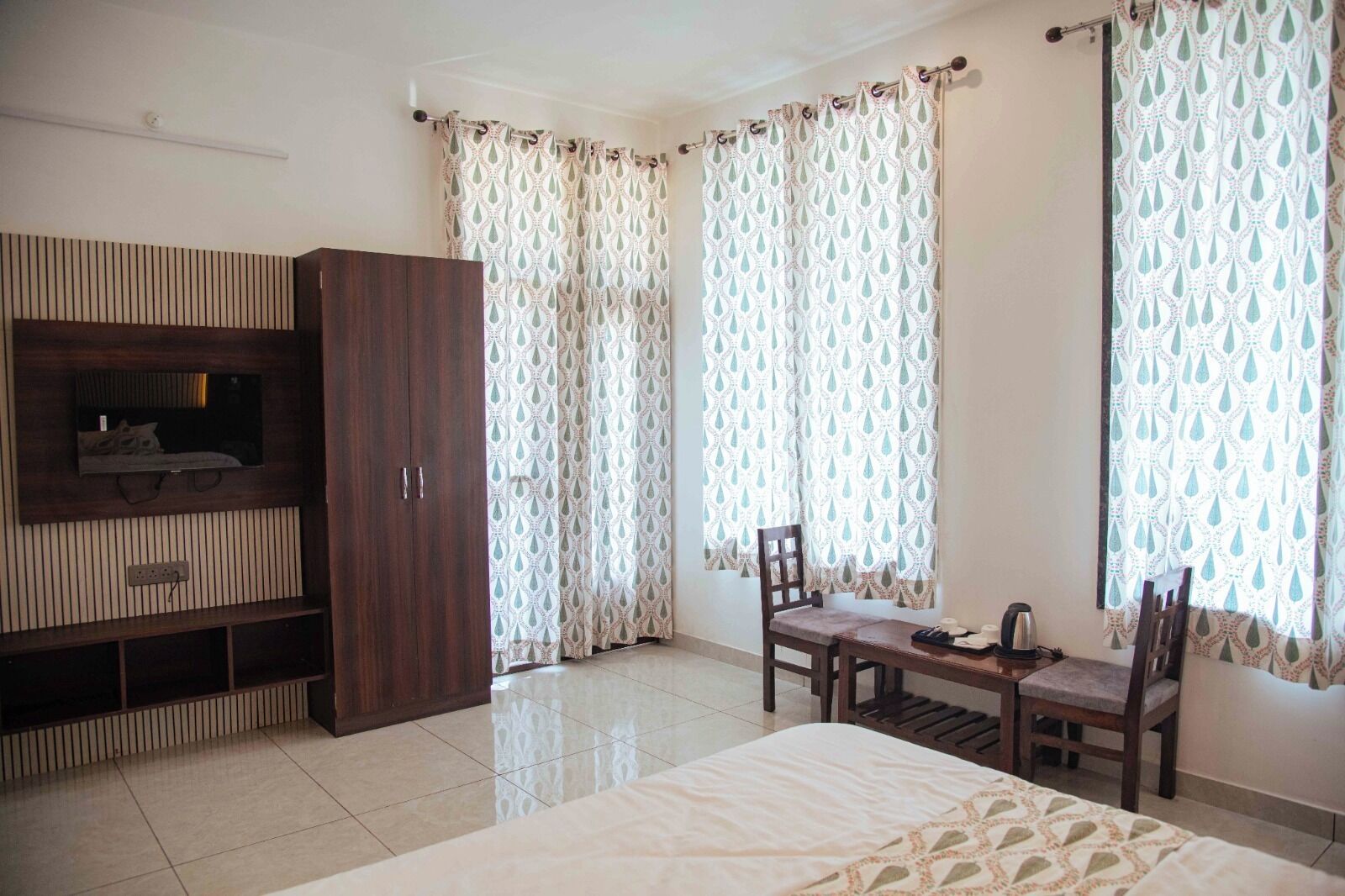 Un dormitorio con cama, televisor montado en la pared, armario de madera y una mesa con sillas.