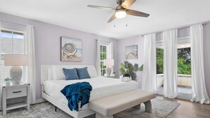 A bedroom with a bed, bedside tables, a ceiling fan, and large windows with curtains. - Serene Matanzas Beach House Half A Mile to Sand (St. Augustine)