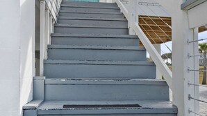 A staircase leading to a turquoise door with a decorative glass panel, white railings, and a clear blue sky in the background. - Serene Matanzas Beach House Half A Mile to Sand (St. Augustine)