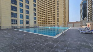 A rooftop swimming pool with a tiled floor, surrounded by high-rise buildings. - Stayshort - Chic Studio in Lago Vista That Sleeps 4 (Dubai)