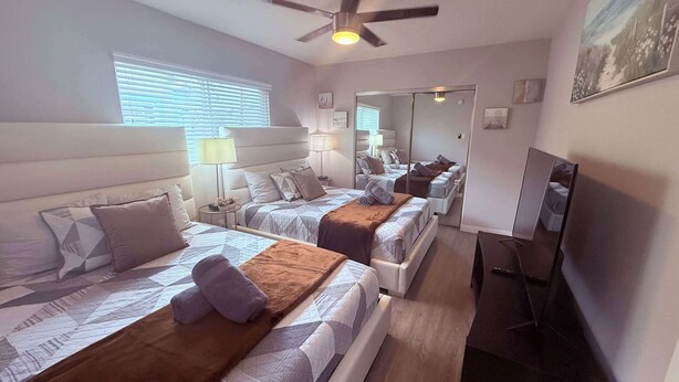 Habitación de hotel con dos camas, ventilador de techo, televisor y un espejo grande.