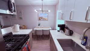 Una cocina moderna con estufa a gas, electrodomésticos de acero inoxidable, comedor con mesa y sillas, y una lámpara colgante.