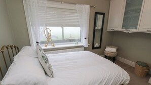A bedroom with a single bed, a window with sheer curtains, a bedside table with a lamp, and a mirror on the wall. - Franbols Cottage (Halifax)