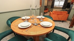 A round wooden dining table with four green upholstered chairs, set for a meal with plates, cutlery, and glasses. - Franbols Cottage (Halifax)