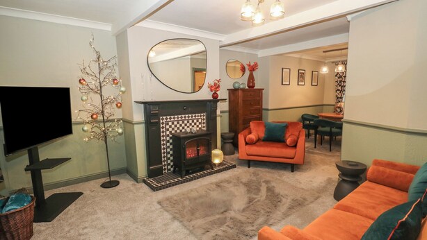 A living room with a fireplace, a television, and a dining area in the background. - Franbols Cottage (Halifax)