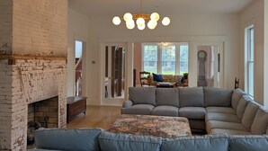 Un salon spacieux avec un grand canapé d’angle, une cheminée et un lustre.