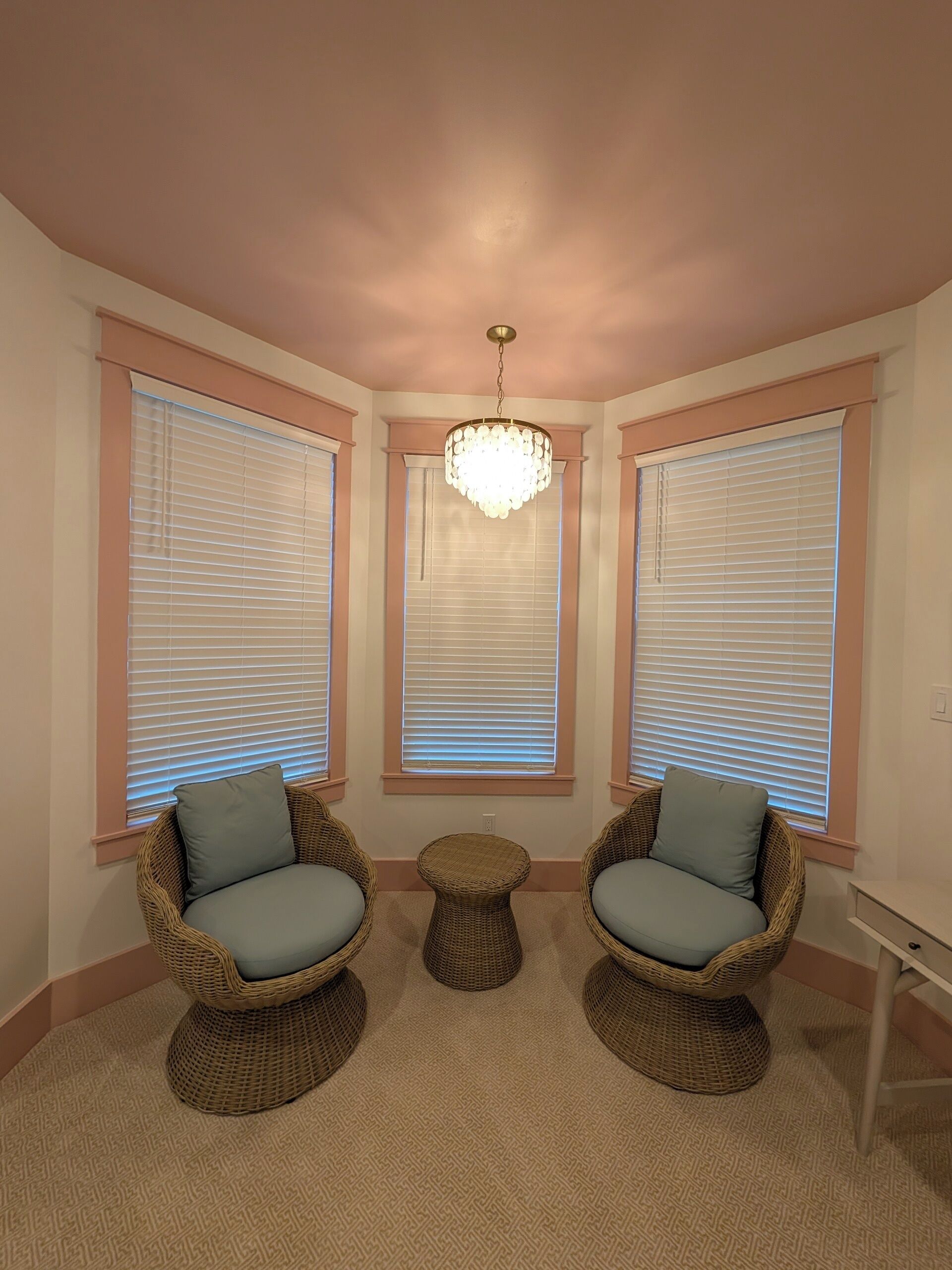 Habitación de esquina con dos sillas de mimbre, una pequeña mesa redonda y un candelabro.