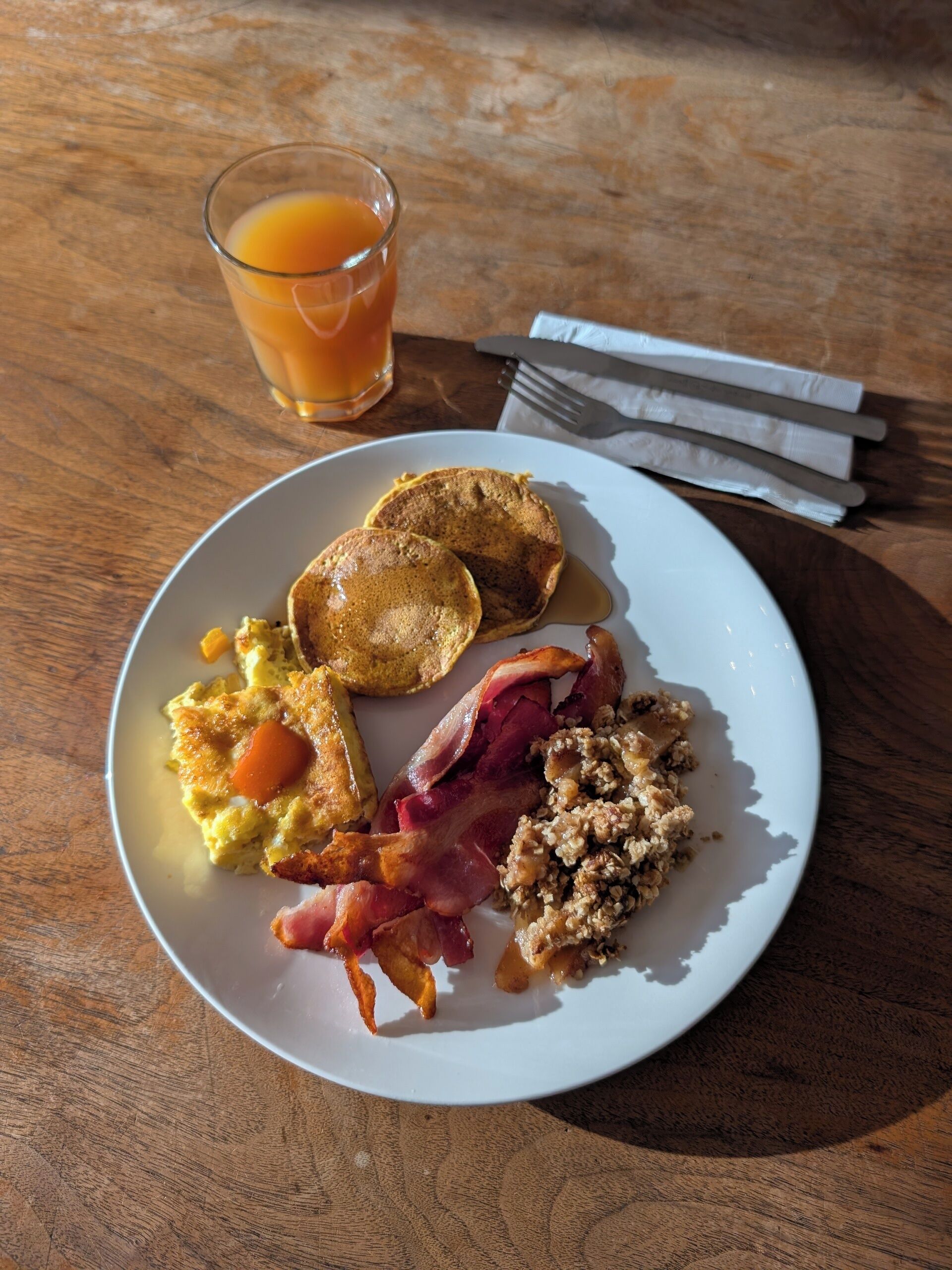 A breakfast plate with eggs, bacon, toast, and a glass of orange juice on a wooden table.