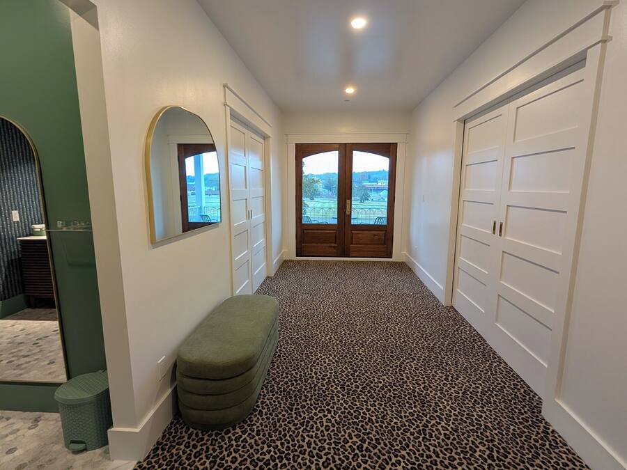 A hallway with a leopard print carpet, white walls, a bench, and a door leading to a balcony with a view.