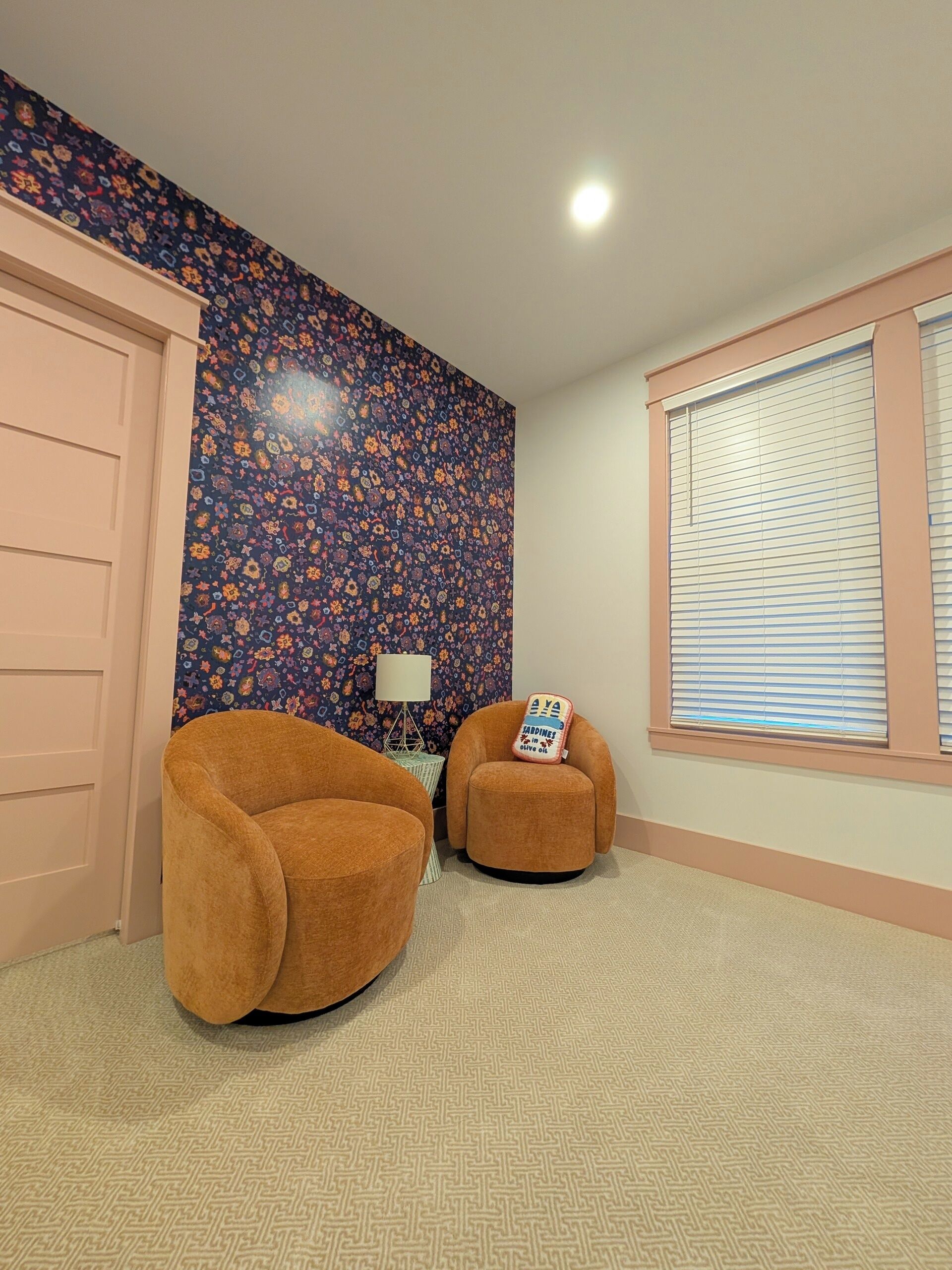 A room with two brown armchairs, a patterned wall, a window with blinds, and a door.