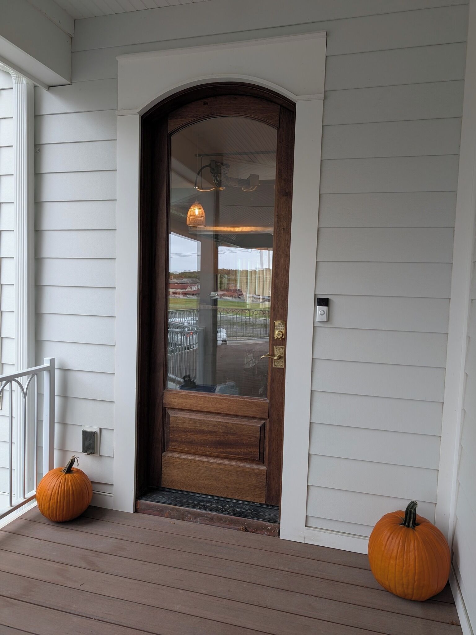 A wooden front door with a glass panel, a porch with wooden steps, and two pumpkins on the ground.