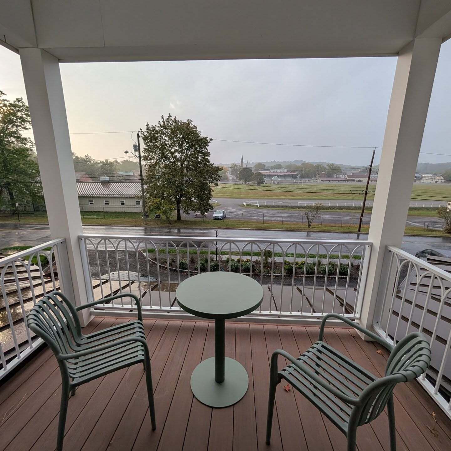 A covered outdoor seating area with a table and two chairs, overlooking a road and distant buildings.