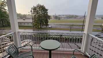 A covered outdoor seating area with a table and two chairs, overlooking a road and distant buildings.